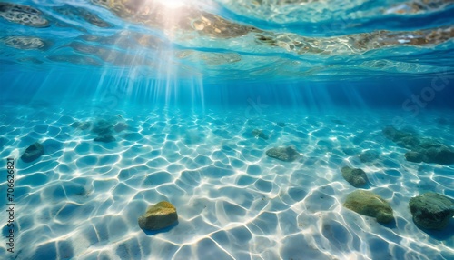 sea water waves texture ripples on water surface light blue ocean water top view clear aqua background sun glow reflection white sand bottom stones underwater tropical island beach © Irene