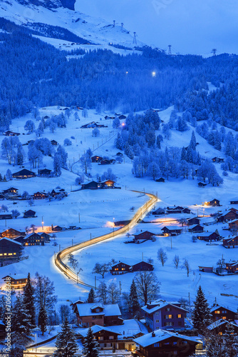 Grindelwald villages of wooden chalets covered with snow in cold winter and the mountain train going through it at the blue hours in Swiss Alps