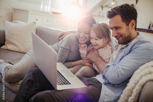 Happy family with young child using laptop on sofa at home