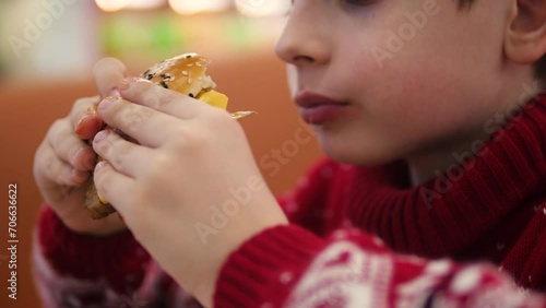 portrait of a hungry Caucasian boy 9 years old eating a delicious burger in a cafe. the child eats a burger. fast food concept. schoolboy snacking on fast food photo