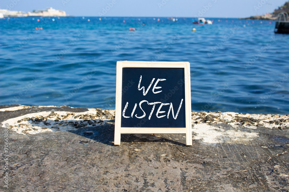 We listen symbol. Concept words We listen on black chalk background. Beautiful sea background. Business and We listen concept. Copy space.