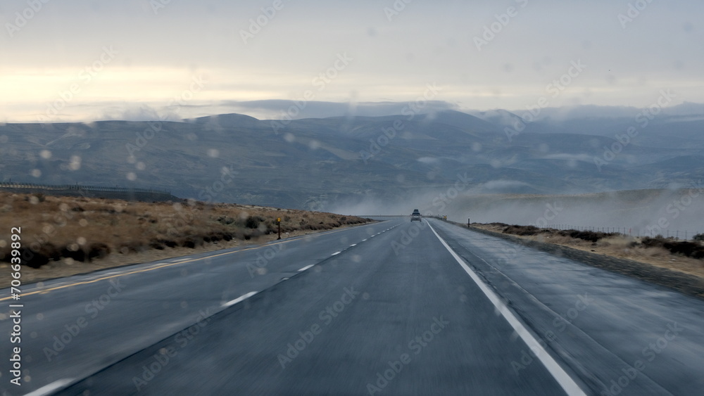 View through car windscreen with raindrops driving on asphalt highway through mountainous landscape on wet, wild day in Washington state, USA