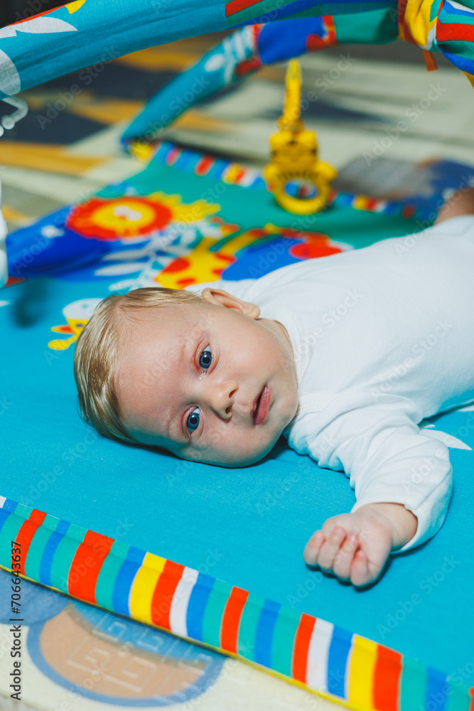 Obraz premium Child development. The baby lies on the developing mat and plays with toys. While playing, the child gets to know the world and learns shapes and colors.
