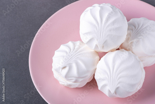 White fluffy marshmallows or marshmallow shells with powdered sugar sprinkles on a pink plate on a grey table