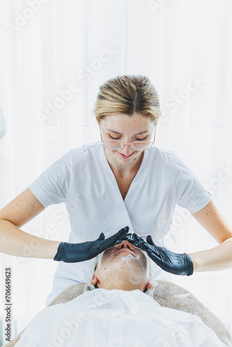 Office of a dermatologist or cosmetologist working with female patients sitting at a massage table, massaging a young woman's face and doing other procedures for facial skin. Facial skin care.