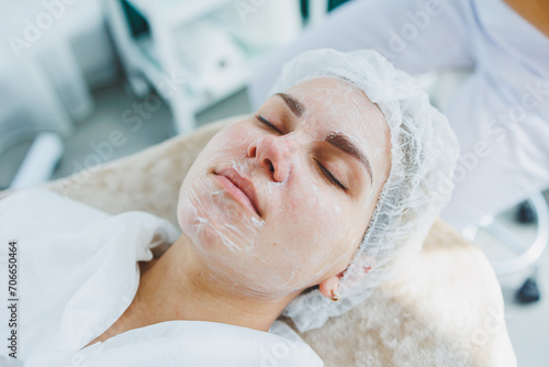 The office of a dermatologist or cosmetologist, a woman lies with a mask on her face. Facial skin care. Close-up of a woman's face with a white cosmetic mask
