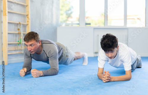 Father and son train abdominal muscles in the gym - perform plank exercise