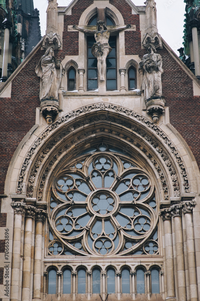 Vintage sculptural composition of the Crucifixion with the coming on the facade of the Church of Olga and Elizabeth in Lviv, Ukraine. Gothic architecture with round stained glass window.