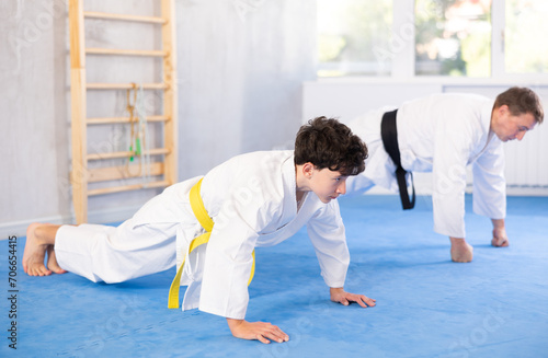 Teenager boy and coach doing muscle stretching before boxing or judo class - doing gymnastic exercise plank