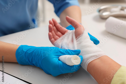 Doctor bandaging patient's burned hand indoors, closeup photo