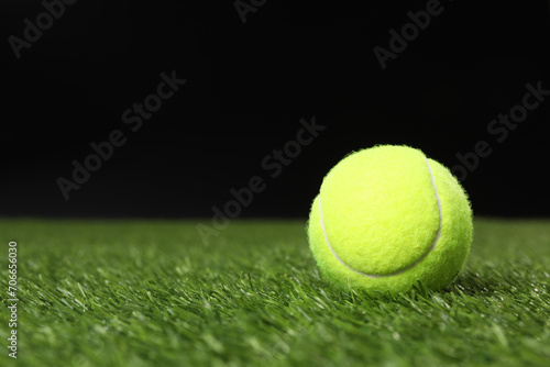 Tennis ball on green grass against black background, space for text