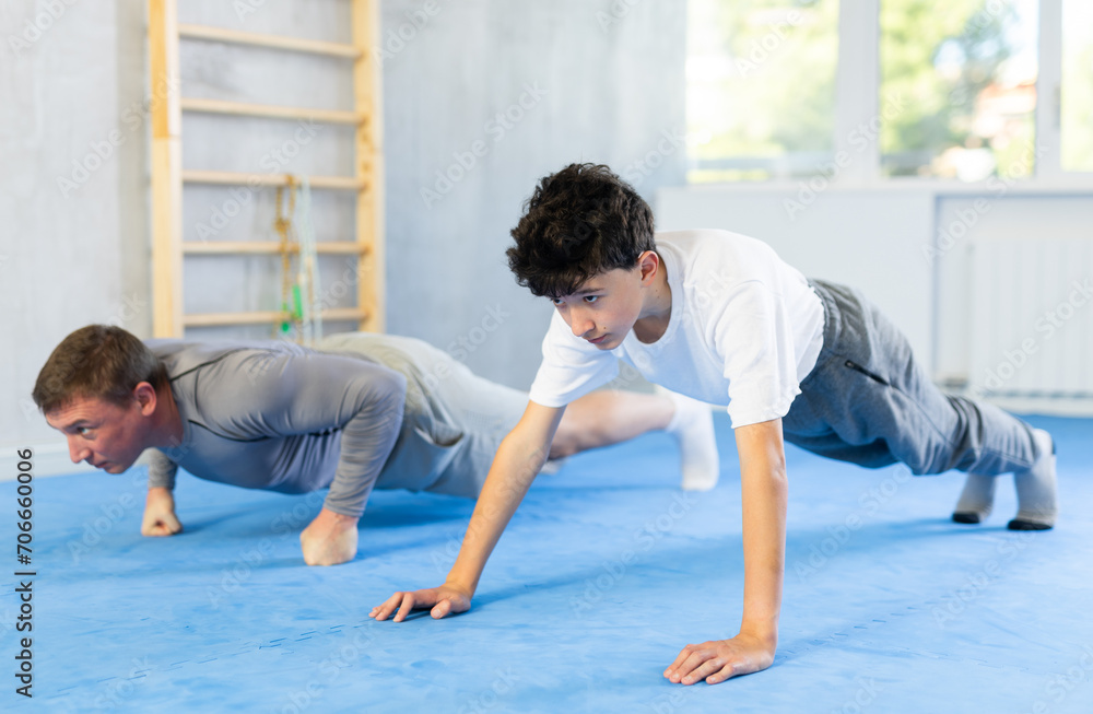 Adult man and teenage boy doing abdominal exercises in gym