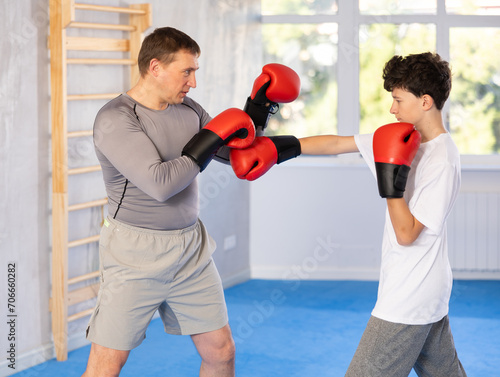 Adult man and boy teenager in boxing gloves boxing in gym © JackF