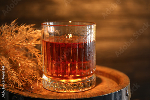 Glass of cold rum on barrel against wooden background