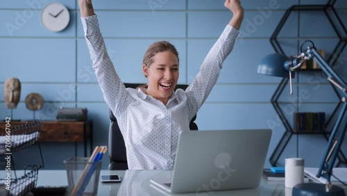 young woman in white shirt sits at table in office with laptop, typing on keyboard concentrated. gets great news of success result, laughs, claps hands, exults of rejoice and satisfaction photo