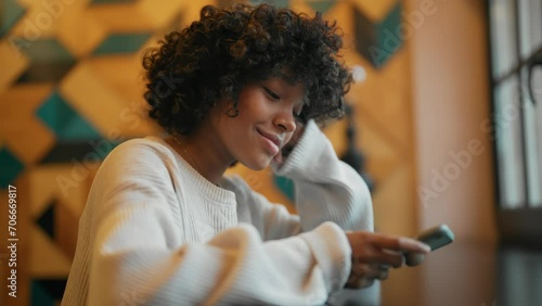 African American girl using smart phone while sitting in cafe. Young woman at cafe using mobile phone Young happy woman use mobile cell phone chat sit alone at table. Freelance office business concept