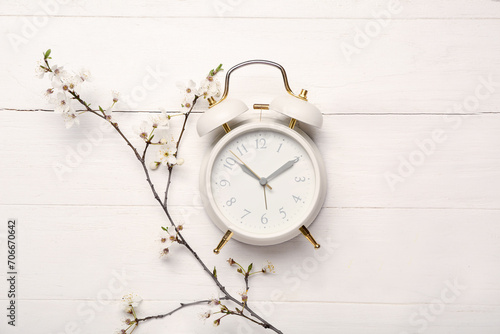 Blooming spring branches and white alarm clock on white wooden background
