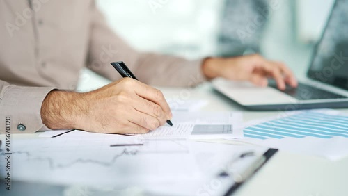Close up. Man's hand fills out a form documents with a pen at a desk at a workplace in business office. A businessman in shirt is doing paperwork, writing, making a tax return, uses a laptop computer photo