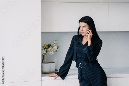 Professional businesswoman in a navy pinstripe suit engaging in a serious conversation on her smartphone with a contemplative expression in a modern office setting photo