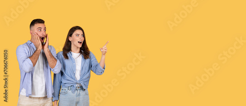 Excited woman pointing away at free space, man shocked, yellow background