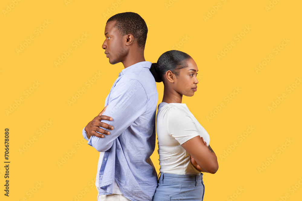 Black couple standing back-to-back, arms crossed, on yellow background Black couple standing back-to-back, arms crossed, on yellow background