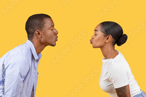 Billede på lærred Black couple puckering for a kiss, profiles facing, on yellow background