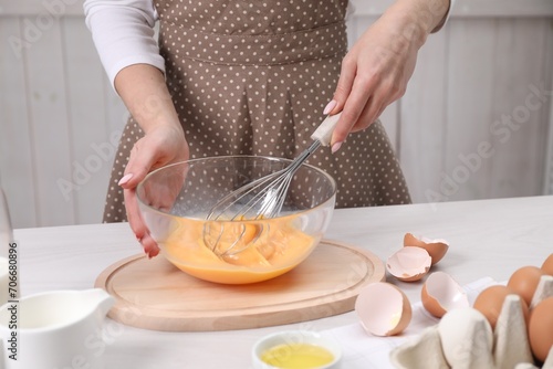 Woman whisking eggs in bowl at table indoors, closeup photo