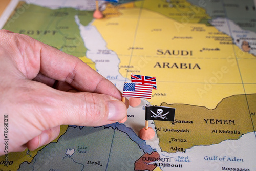This evocative image captures a hand placing pins adorned with the flags of the USA, UK, and a pirate insignia onto a map of the Red Sea region. It symbolically represents the intricate geopolitical