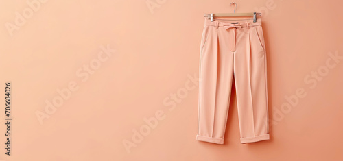 peach-colored trousers hang on a hanger on a peach background