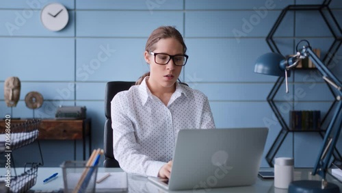 young woman in white shirt and eyeglasses sit at table desk in office, working at laptop. frustrated and worried, frowns, gives up and closes computer to have a break and breath out.