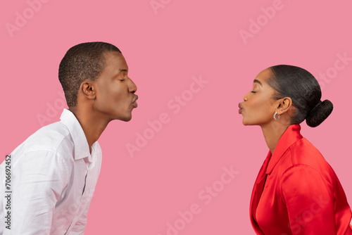 Black man and woman in profile facing each other, puckering lips on pink photo