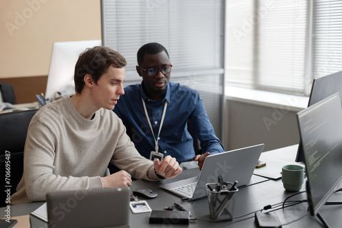 Fotografie Caucasian male junior IT specialist sitting at table and explaining new cybersec