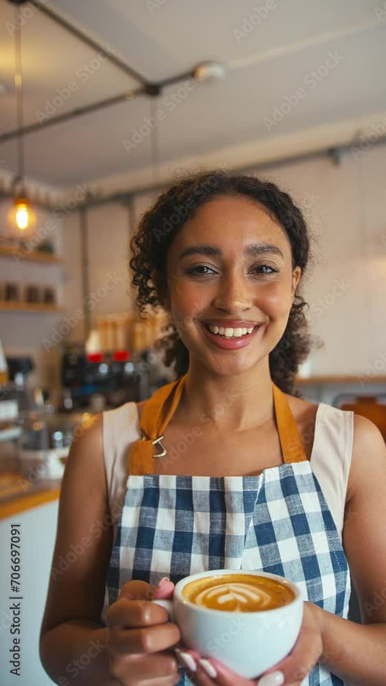 Vertical video portrait of confident smiling young woman wearing apron working or owning coffee shop holding coffee cup - shot in slow motion Vertical video portrait of confident smiling young woman wearing apron working or owning coffee shop holding coffee cup - shot in slow motion