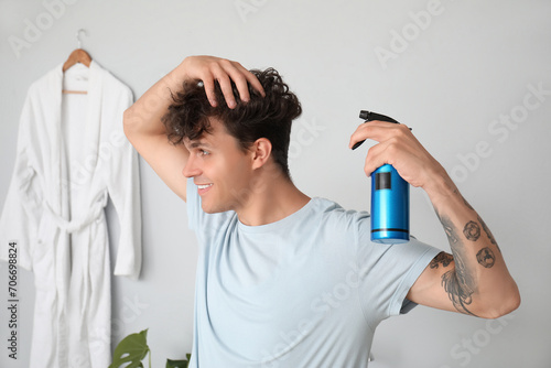 Fotografie Handsome young man with tattoo applying hair spray on his curly hair in bathroom