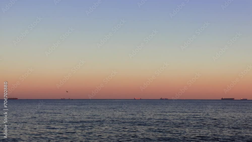 Sunset over calm sea, ships on roadstead bask in sunset glow. Tranquil sea waves at sunset, ships anchored in roadstead. Roadstead ships illuminated by sunset, calm sea waves Sunset over calm sea, ships on roadstead bask in sunset glow. Tranquil sea waves at sunset, ships anchored in roadstead. Roadstead ships illuminated by sunset, calm sea waves