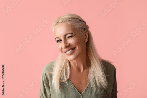 Mature woman winking on pink background, closeup photo