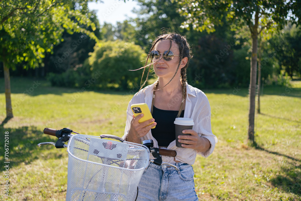 Smiling young hipster woman with bicycle using mobile phone in city park Smiling young hipster woman with bicycle using mobile phone in city park