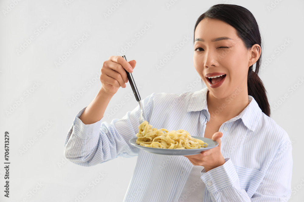 Young Asian woman eating tasty pasta on light background Young Asian woman eating tasty pasta on light background