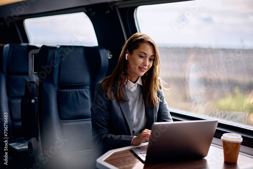 Fotografija Smiling businesswoman works on laptop while commuting by train.