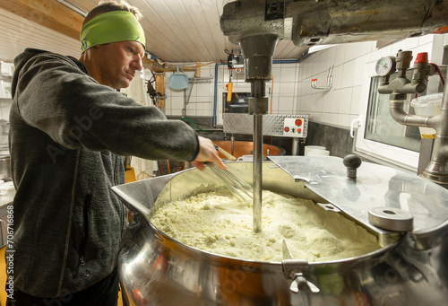 A focused cheese maker stirs curdled milk in a large vat engaged in the traditional craft of cheese production