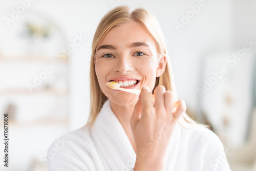 Portrait of pretty blonde woman attentively cleaning her teeth indoors