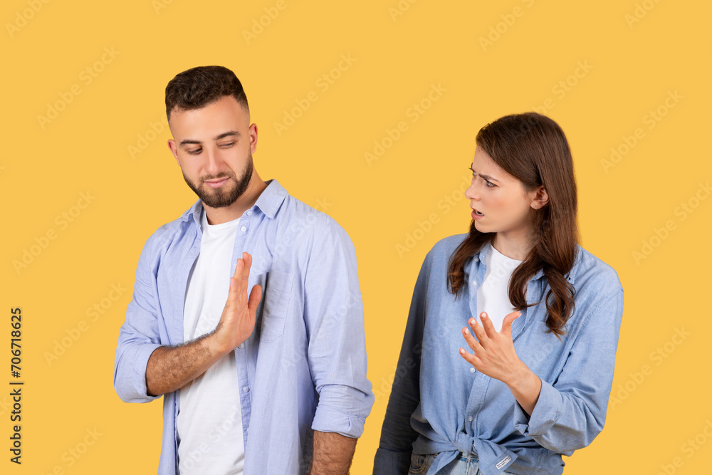 Man showing stop gesture to arguing woman, yellow background Man showing stop gesture to arguing woman, yellow background