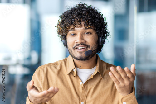 Canvas Print Web camera view, online video call, young man smiling and looking into camera with headset phone for video call, businessman inside office, selling and advising consumers, support service