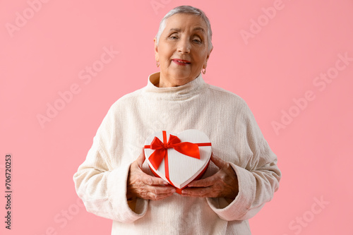 Senior woman with gift box on pink background