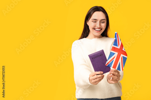 Pretty young woman with UK flag and passport on yellow background. Immigration concept photo
