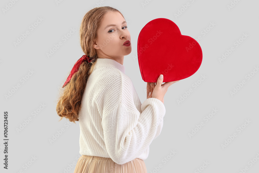 Young redhead woman with ponytail and scrunchy holding heart on light background Young redhead woman with ponytail and scrunchy holding heart on light background