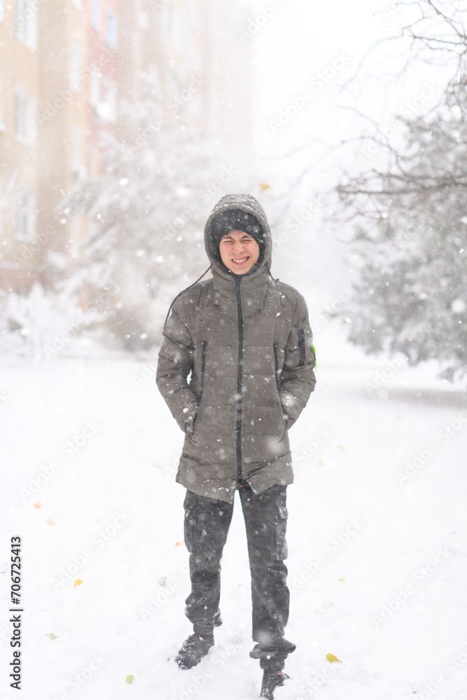 Fototapeta premium A boy walks along a snowy street, it is snowing, blizzard and frost on a winter day