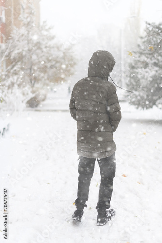 A boy walks along a snowy street, it is snowing, blizzard and frost on a winter day © soleg