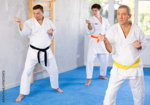 Elderly man in kimono trains karate techniques in group in studio