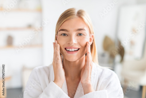 Portrait of blonde lady touches cheeks enjoys morning skincare indoor